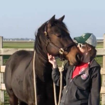AC on a sunny day standing next to her horse, Aspen, giving her a kiss on the side of her muzzle